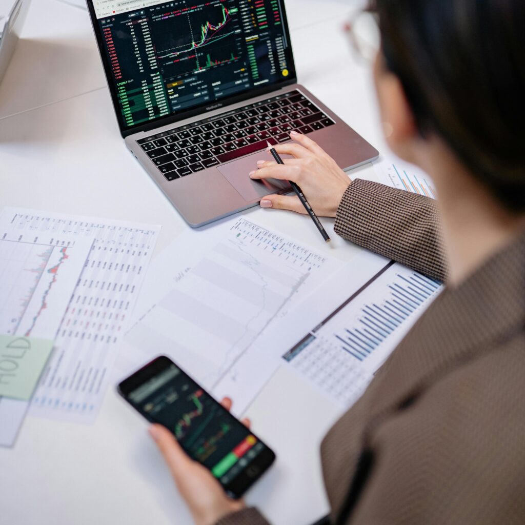pexels-photo-7693229-7693229 A business professional analyzing stock charts on a laptop and smartphone at the office.